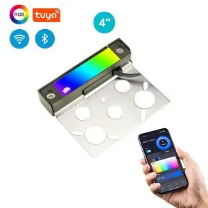 A 4" brass hardscape light with stainless steel mounting brackets and smart color changing options via wireless connectivity, as denoted by a hand holding a phone with the options available visible on screen at the bottom right and icons showing the various functionalities in the top left of the image.